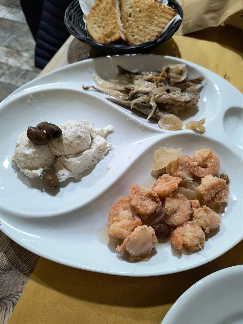 Antipasto di mare in un piatto a scomparti: baccalà mantecato con olive, sardoni in savor e gamberi.
