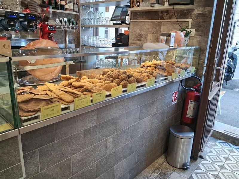 La vetrina del banco con melanzane, zucchine e ombolo impanati, polpette, la macchina del caffè e le spine della birra.