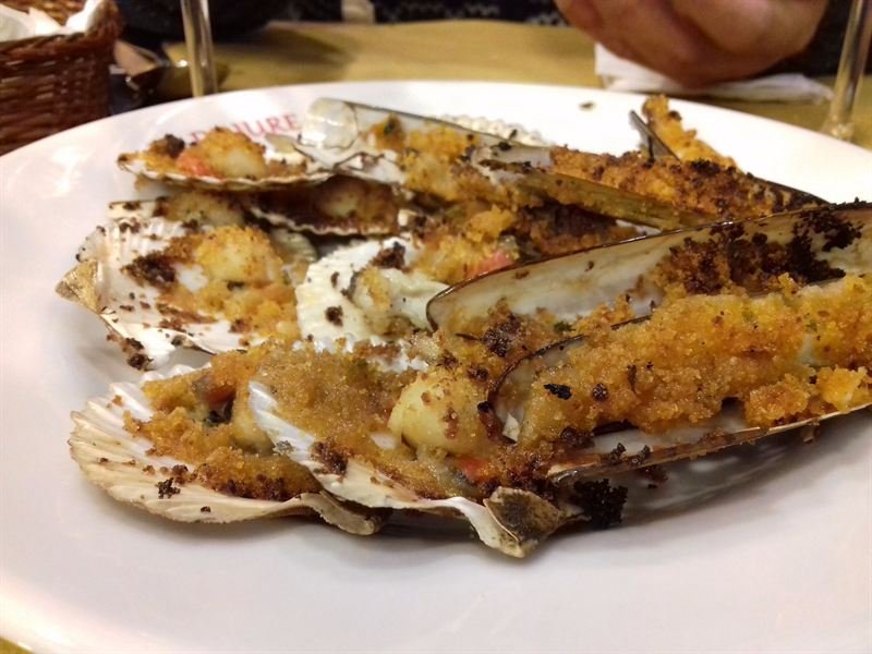 Capesante e cannolicchi gratinati con pangrattato dorato, nel piatto con la scritta La De Jure.