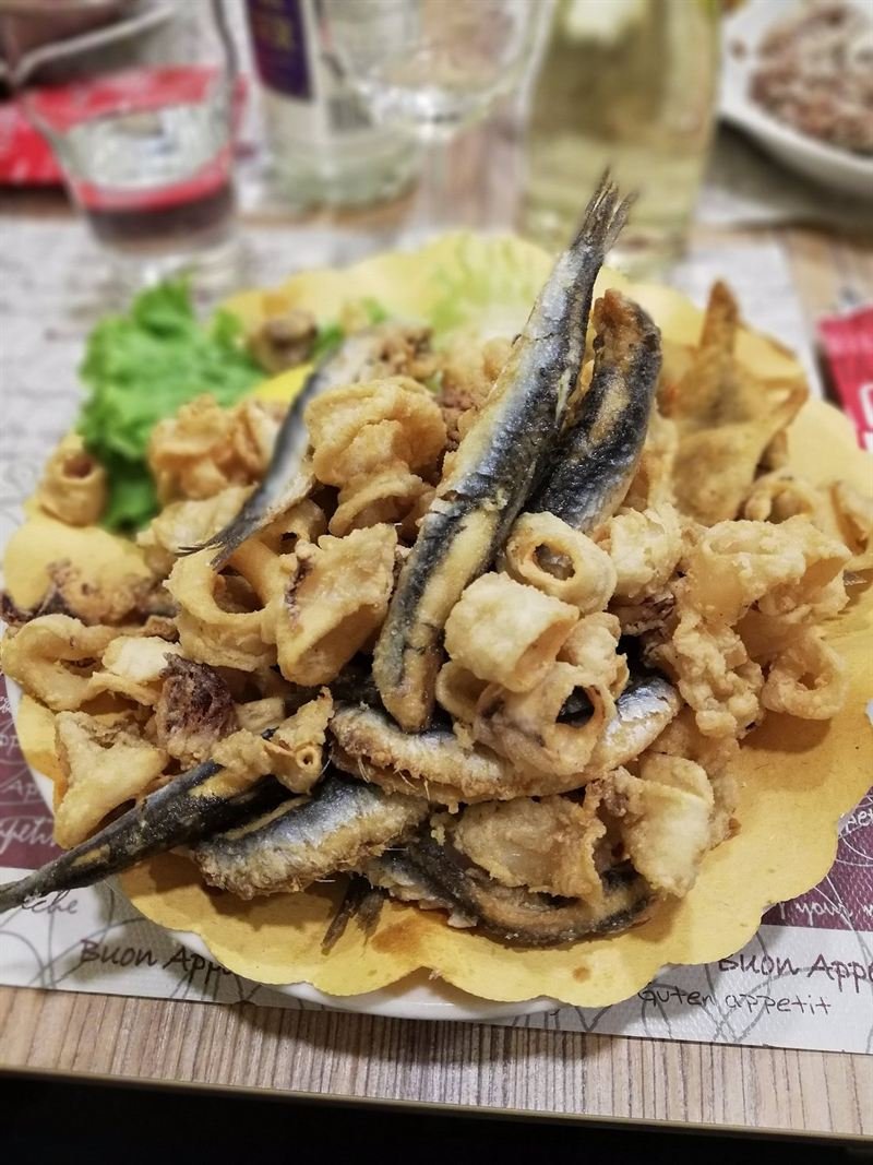 Frittura di calamari e pesce azzurro su carta, con insalata.