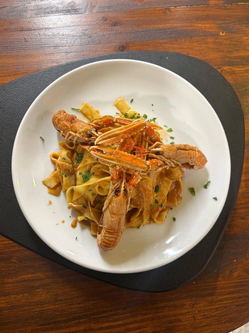 Tagliatelle agli scampi viste dall’alto, su un sottopiatto nero e un tavolo di legno.